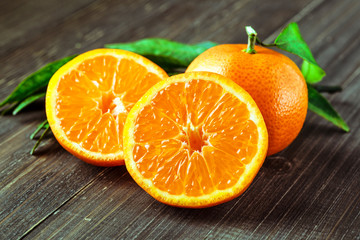 Ripe Mandarin fruit peeled open and place on old rustic look timber with group of mandarin fruits and leaves out of focus on the background