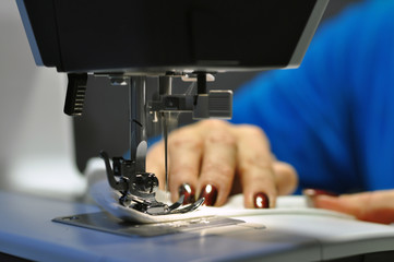Sewing machine. At work, a girl with a beautiful manicure in her hands.