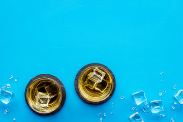 Whiskey near ice cubes on blue background top-down frame copy space
