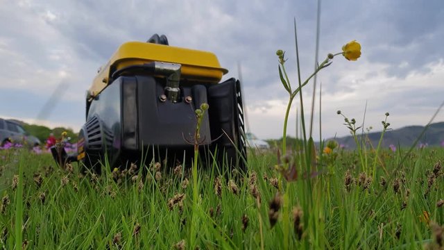Close up of gas diesel mobile portable electricity generator work on grass. Gasoline fuel powered portable generator give electric energy current for camping. Background: grass, tent, car. Outdoor.