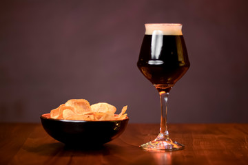 Glass of dark beer with chips on the counter table in bar. Alcohol drink. Food photography concept, copy space.
