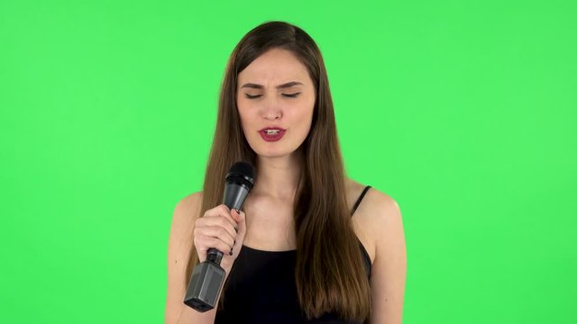 Attractive girl sings into a microphone and moves to the beat of music. Green screen