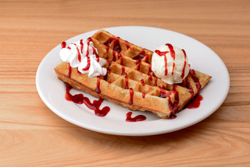 Plate of belgian waffles with ice cream and fruit strawberry caramel sauce on wooden table background