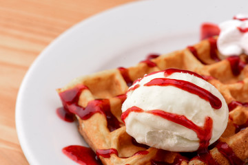 Plate of belgian waffles with ice cream and fruit strawberry caramel sauce on wooden table background