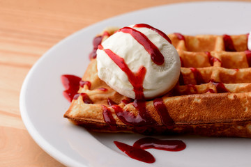 Plate of belgian waffles with ice cream and fruit strawberry caramel sauce on wooden table background