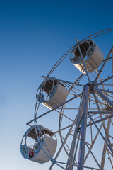 Part of a ferris wheel with round cabins decorated with ornaments against a blue sky.