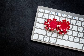 Online poker. Chips near keyboard on black background top-down copy space