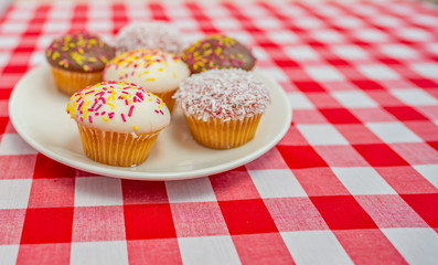  Selective focus on a cup cake on a plate of six cupcakes on a plain white plate on a red and white checked table cloth