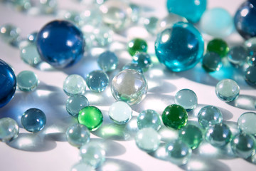 A lot of colorful shiny marble balls on white background. Blue, green transparent glass balls close up. Abstract background.