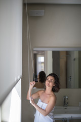 Pretty, young woman lowering the interior shades/blinds in her modern interior apartment