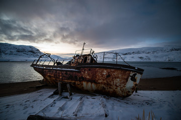 abandoned, already rotten skeletons of ships lying on the coast of the Arctic ocean against the background of a pink sunset