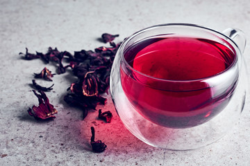 Hibiscus tea in a glass cup on a stone background with scattered petals. © Nataliia Sirobaba