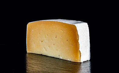 a piece of solid cheese in a white wrapper on a black background close-up