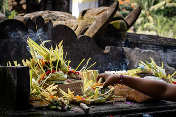A hand placing burning incense in an offering at a Balinese temple