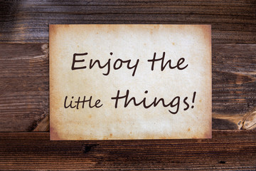 Old Grungy Paper With English Text Enjoy The Little Things. Wooden Background
