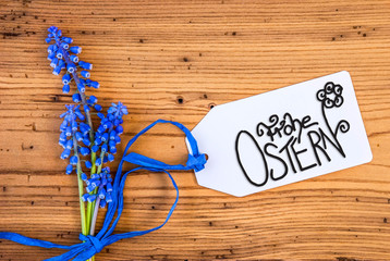 Label With German Calligraphy Frohe Ostern Means Happy Easter. Blue Spring Hyacinth Flower On Rustic Wooden Background.