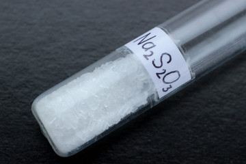 White crystals of sodium thiosulfate in test tube, on a black background, the substance is used in...