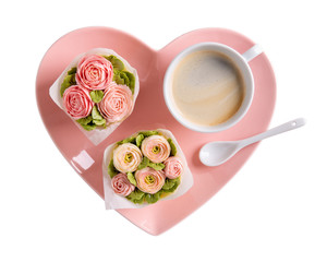 Flower cupcakes and cup of coffee on heartshaped plate isolated on white background. Beautiful sponge cup cakes decorated with buttercream roses.