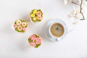 Obraz na płótnie Canvas Flower cupcakes and cup of coffee on white background. Beautiful sponge cup cakes decorated with buttercream roses. Top view, copy space.