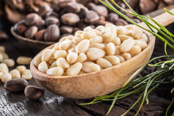 Pine nuts in the spoon and pine nut cone on the wooden table. Organic food.