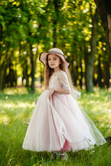 A little beautiful girl in a dress and a hat in the park smiles.