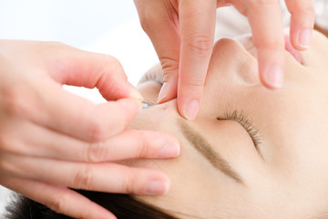 鍼灸院で顔に鍼を打たれる女性と施術者の手のアップ
