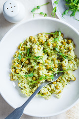Green risotto with broccoli, green peas and sprouts in white plate, top view. Healthy vegan food concept.