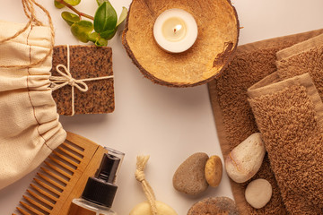 Fototapeta na wymiar Spa and wellness concept, natural coffee scrub soap in eco bag, oil cosmetics spray, peeling sand stone, towel,wooden haircomb. Beige dayspa set.Brown pastel bathroom accessories and products top view