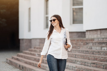 Fototapeta premium Portrait of One Fashionable Girl Dressed in Jeans and White Shirt Holding Laptop, Freelance Worker, Business Lady, Woman Power Concept
