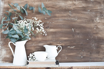 jug with white flowers and eucalyptus branches on the background of a shabby wooden wall.