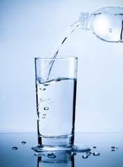 Pouring fresh pure water from bottle into a glass on the table with water drops, Healthcare and beauty hydration concept