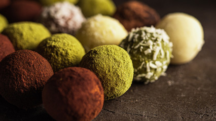 Colorful homemade truffles coated in cocoa powder, matcha tea powder, shredded cococnut on dark background. Copy space for text or design, banner.