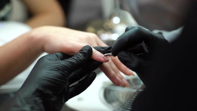 Nail master in rubber gloves makes professional manicure to girl in beauty salon, close-up. Shooting in slow motion.