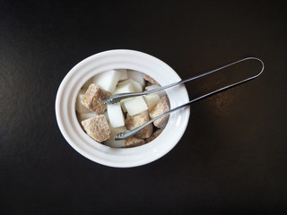 Sugar-basin with cubes of white and brown sugar on black background