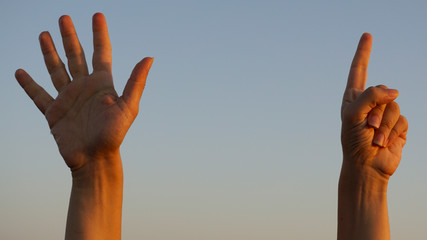 Hands doing / showing number six gesture symbol on blue summer sky nature background. Gesturing number 6. Number six in sign language. Sixth and counting down six concept. Six fingers up. Space for ad
