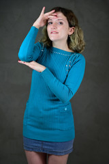 Portrait of a pretty student girl with beautiful curly hair is standing in front of the camera on a gray background. Concept vertical photo of a young woman with emotions in a blue dress.