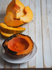 Cooking pumpkins. Home cooking, natural food for vegetarians. Traditional autumn pumpkin dishes. Grilled grilled pumpkin with spices on a background of raw pumpkin on a white wooden table.