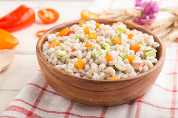 Pearl barley porridge with vegetables in wooden bowl on a white wooden background and linen textile. Side view, selective focus.