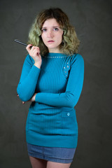Fototapeta premium Concept vertical photo of a young woman with emotions in a blue dress. Portrait of a pretty student girl with beautiful curly hair is standing in front of the camera on a gray background.