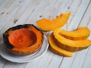Cooking pumpkins. Home cooking, natural food for vegetarians. Traditional autumn pumpkin dishes. Grilled grilled pumpkin with spices on a background of raw whole pumpkin on a wooden background.