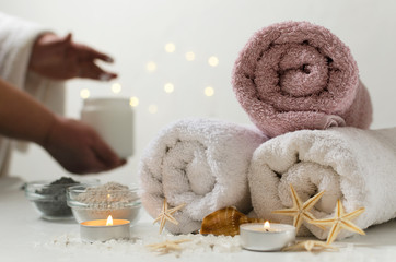 Spa salon concept. Woman with bowl of moisturizing cream, towels and glass bowls full of body clay, candles, sea salt on the white surface