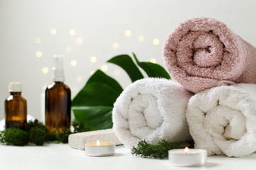 Fototapeta na wymiar Natural spa procedures. Fresh tropical leaves, towels, candles and glass bottles of oil for body on the white surface against bokeh lights
