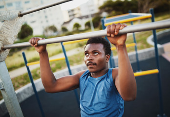 Fototapeta na wymiar Portrait of determined sporty young african american man performs pull ups exercises to strengthen muscles at outdoors gym park