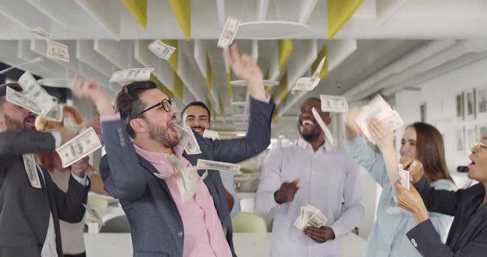 Group of bank workers having fun and throwing money while rejoicing good deal. Cheerful young employees dancing and celebrating big profit in modern office working zone.