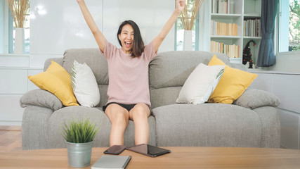 Obraz premium Young Asian teenager woman watching TV at home, female feeling happy lying on sofa in living room. Lifestyle woman relax in morning at home concept.