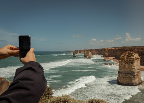 Tourist taking pictures of scenic 12 apostles rock formations and cliffs in australia