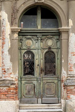 Old weathered decorated door with wrought iron ornaments, on an old brick building