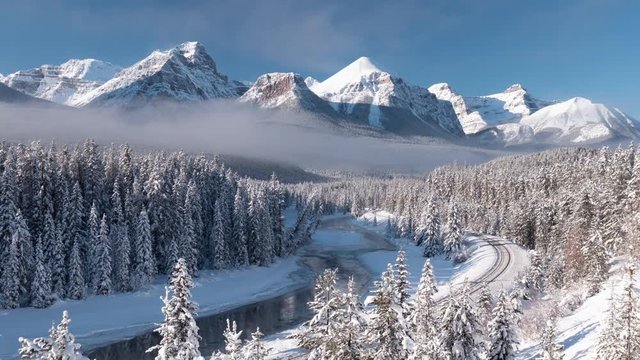 Snowy mountain time-lapse of Morant's curve in Banff National Park which features mountains, forests, a river, and railroad track in a winter wonderland.