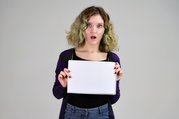 Naklejka premium Concept horizontal photo of a young woman with emotions in a dark jacket standing in front of the camera on a white background. Portrait of a student girl with a folder in her hands with fluffy hair.