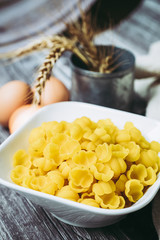 Pâtes crues dans un bol en céramique blanc et oeufs sur la table de cuisine